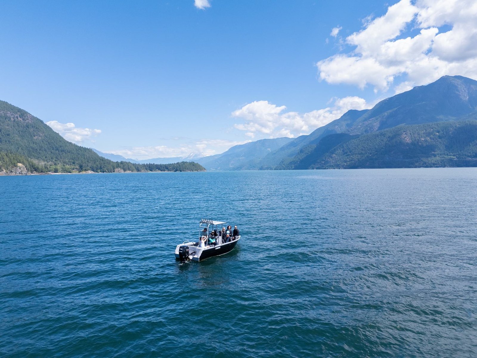 A small boat crossing the blue water of Howe Sound beneath mountains
